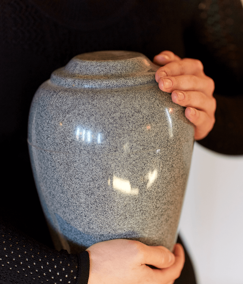 Hands holding a smooth, gray stone urn.